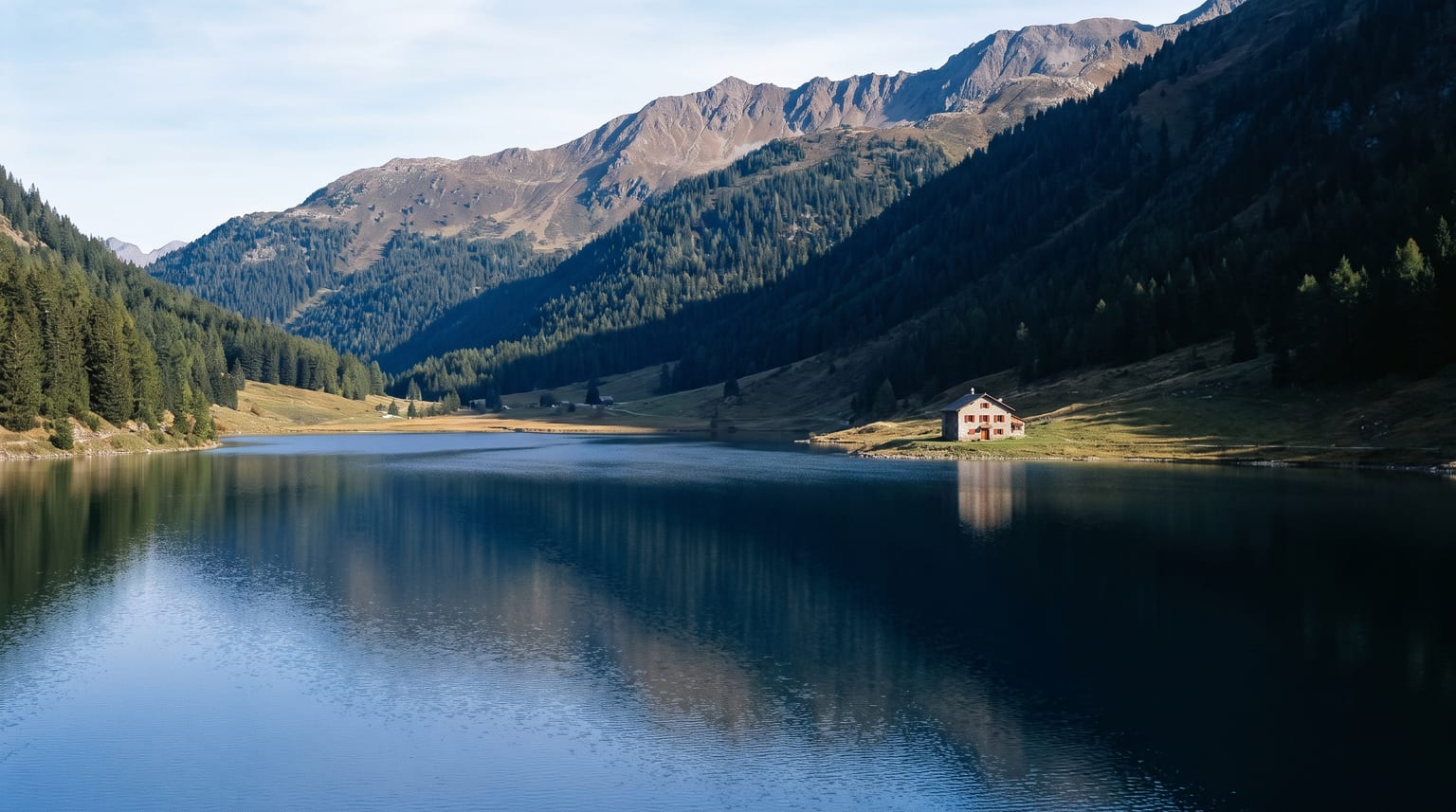 Schweizer Bergsee am Morgen, dunkelblaues Wasser, ein Bauernhaus mit roten Fensterläden am Ufer