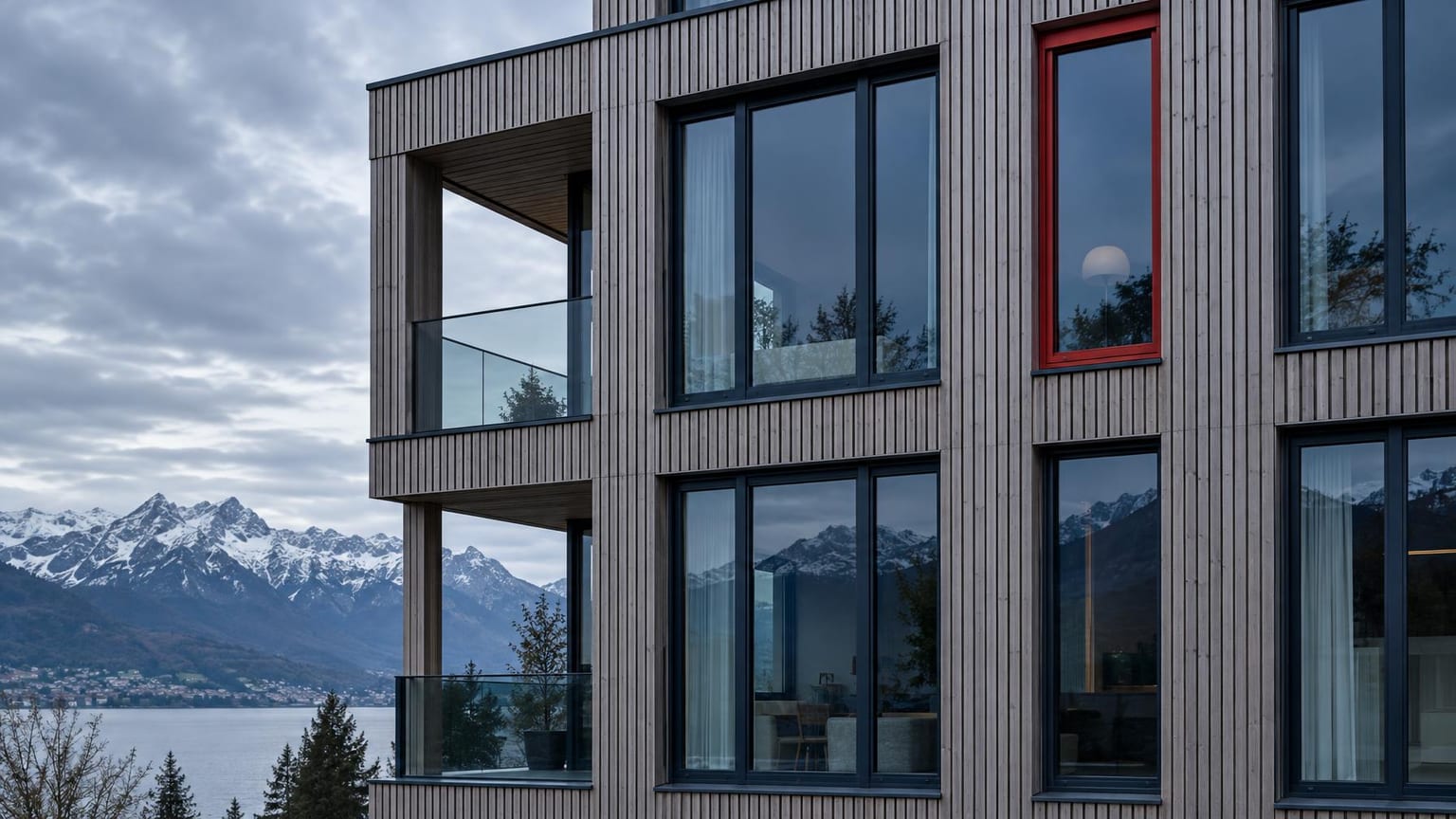 Moderne Schweizer Holz- und Glasfassade unter bedecktem Himmel, ein einzelner roter Fensterrahmen