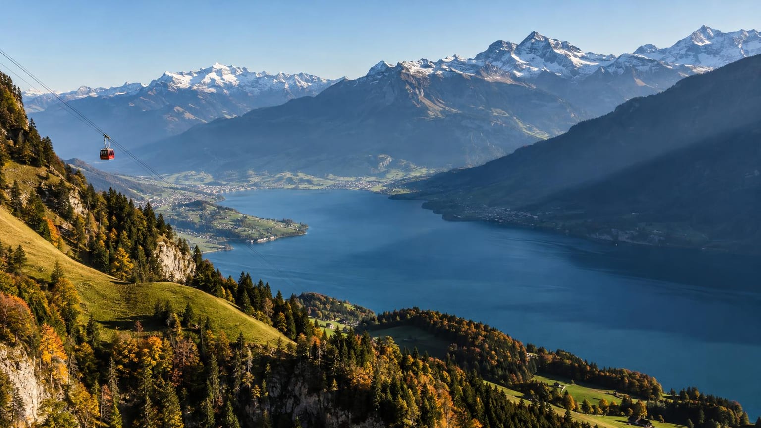 Weite Berglandschaft am Morgen mit tiefblauem See und Bergschatten, in der Ferne eine einzelne rote Luftseilbahnkabine